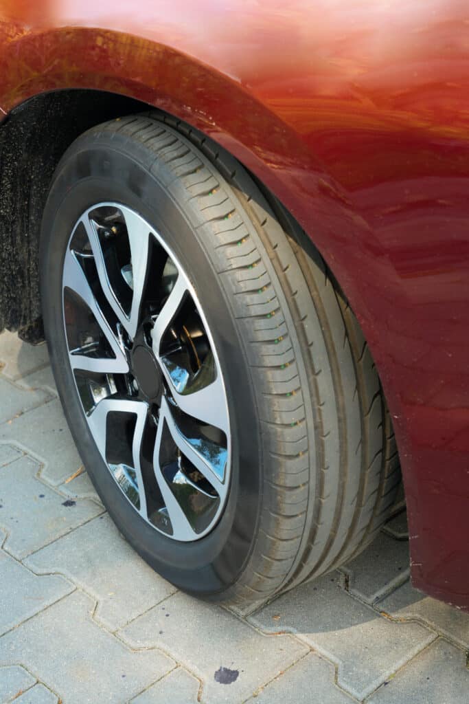 Roue d'une voiture rouge avec jante bicolore noire et argent, sur des pavés