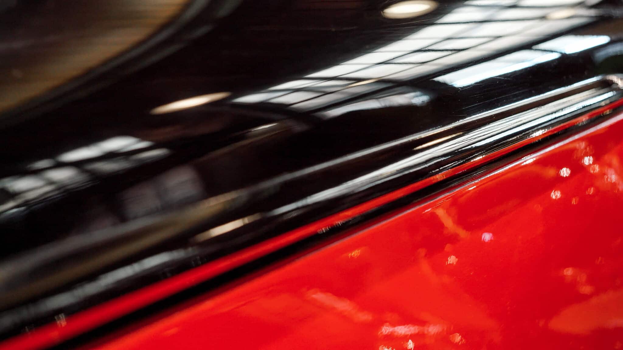 Gros plan sur une carrosserie lustrée noire et rouge, reflets lumineux sur la peinture