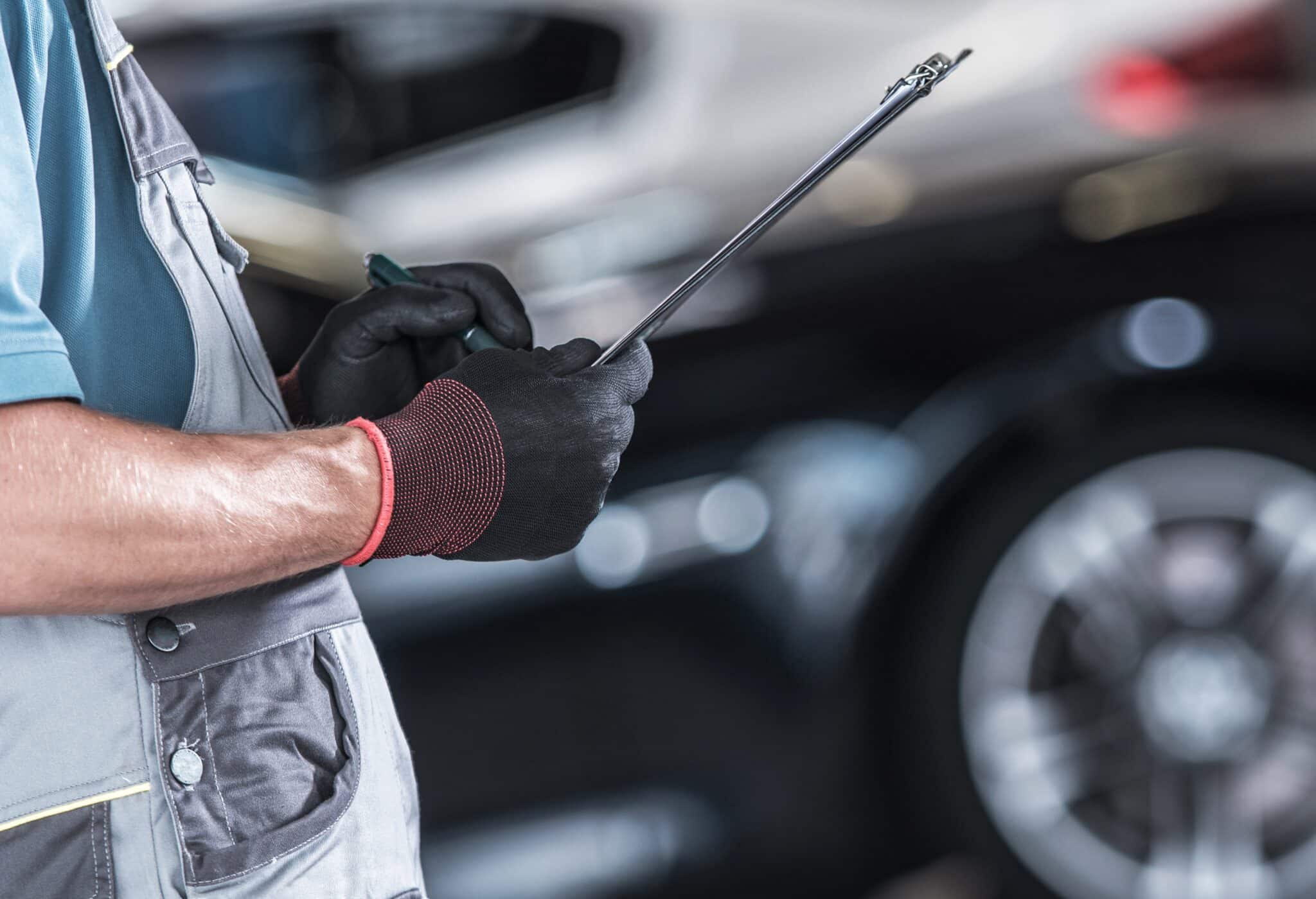 Technicien ganté tenant un porte-bloc à côté d'une voiture dans un atelier