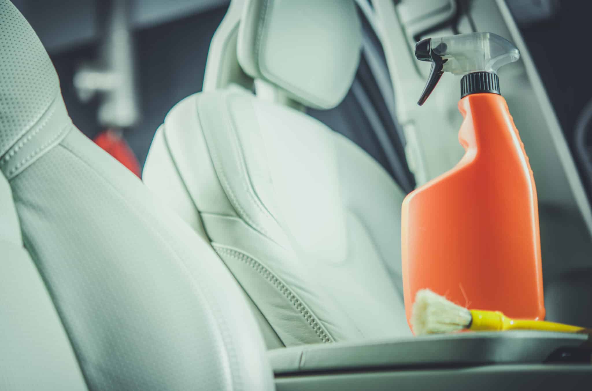 Flacon pulvérisateur orange et pinceau posés sur l'accoudoir entre des sièges en cuir gris clair