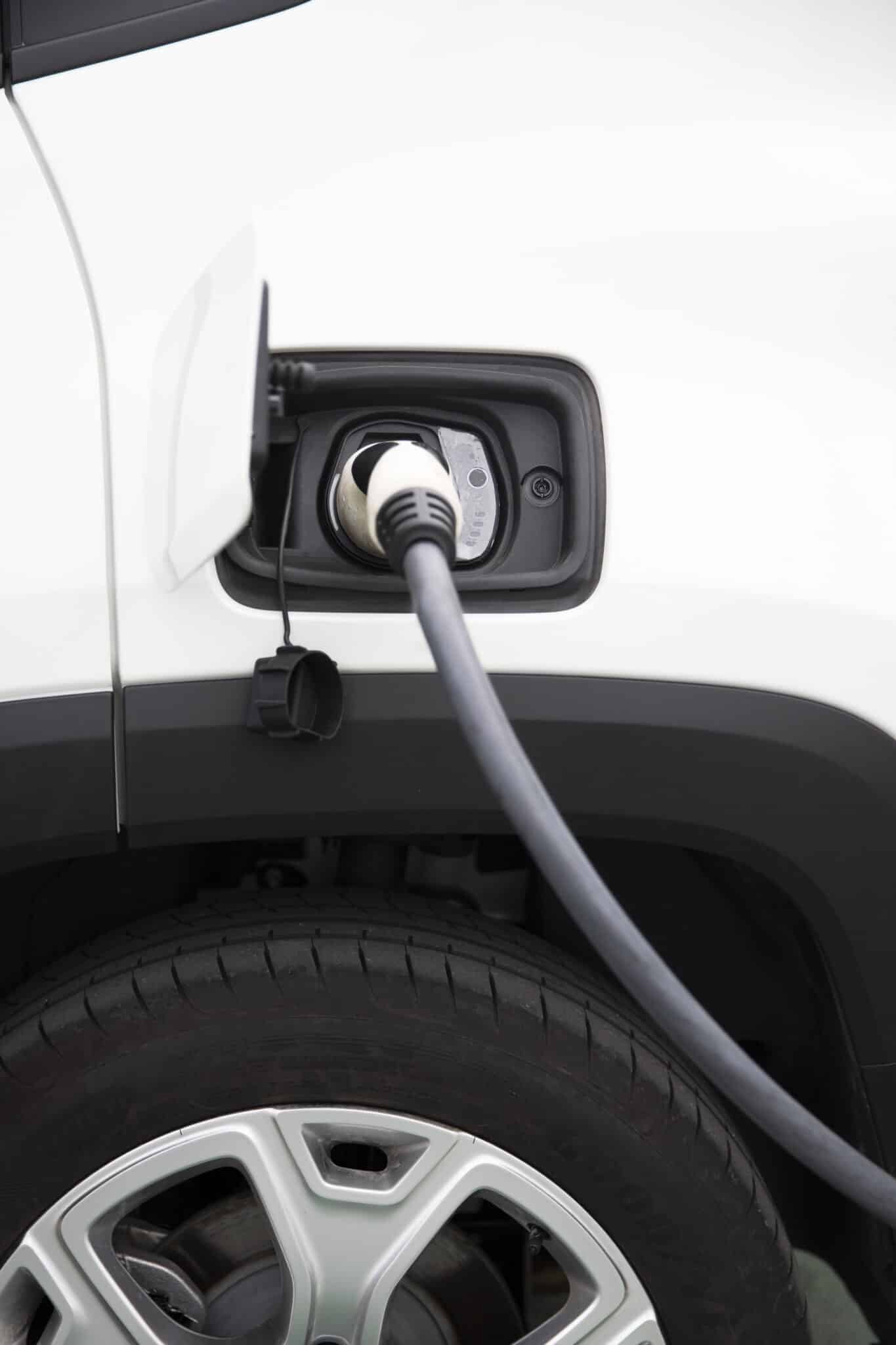 Câble de recharge branché dans la prise d'une voiture blanche, au-dessus d'une roue