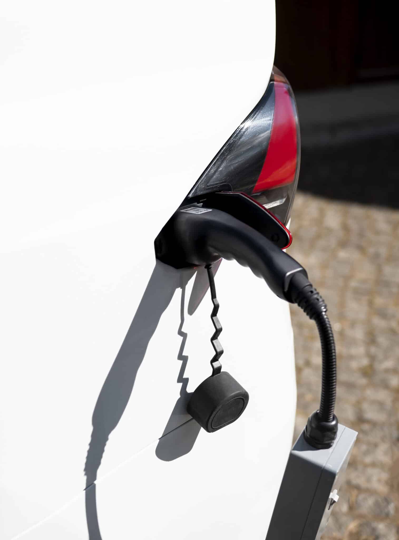 Prise de recharge branchée sur le flanc d'une voiture blanche, capuchon noir pendant au câble