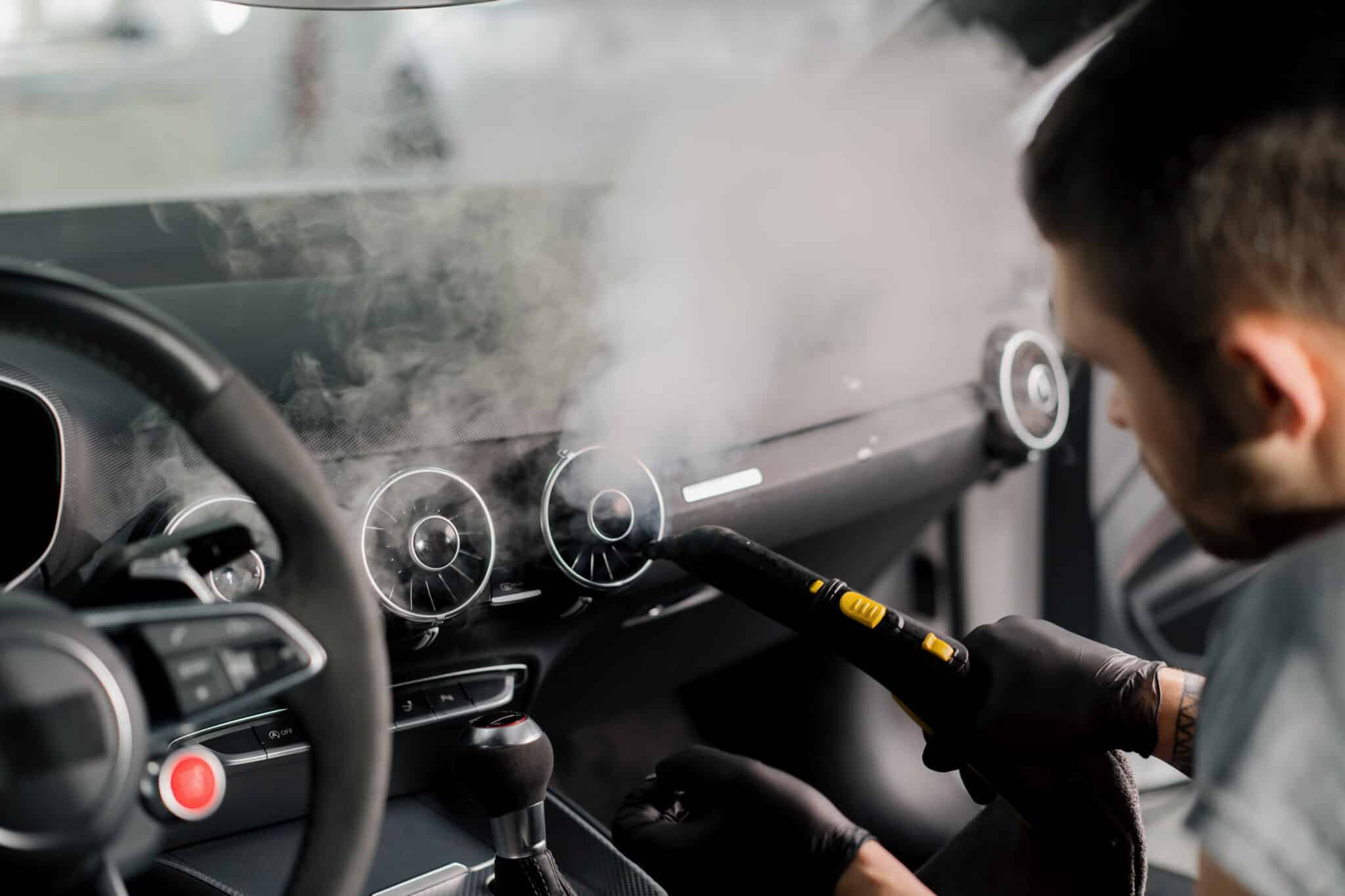 Homme ganté passant un nettoyeur vapeur sur le tableau de bord d'une voiture