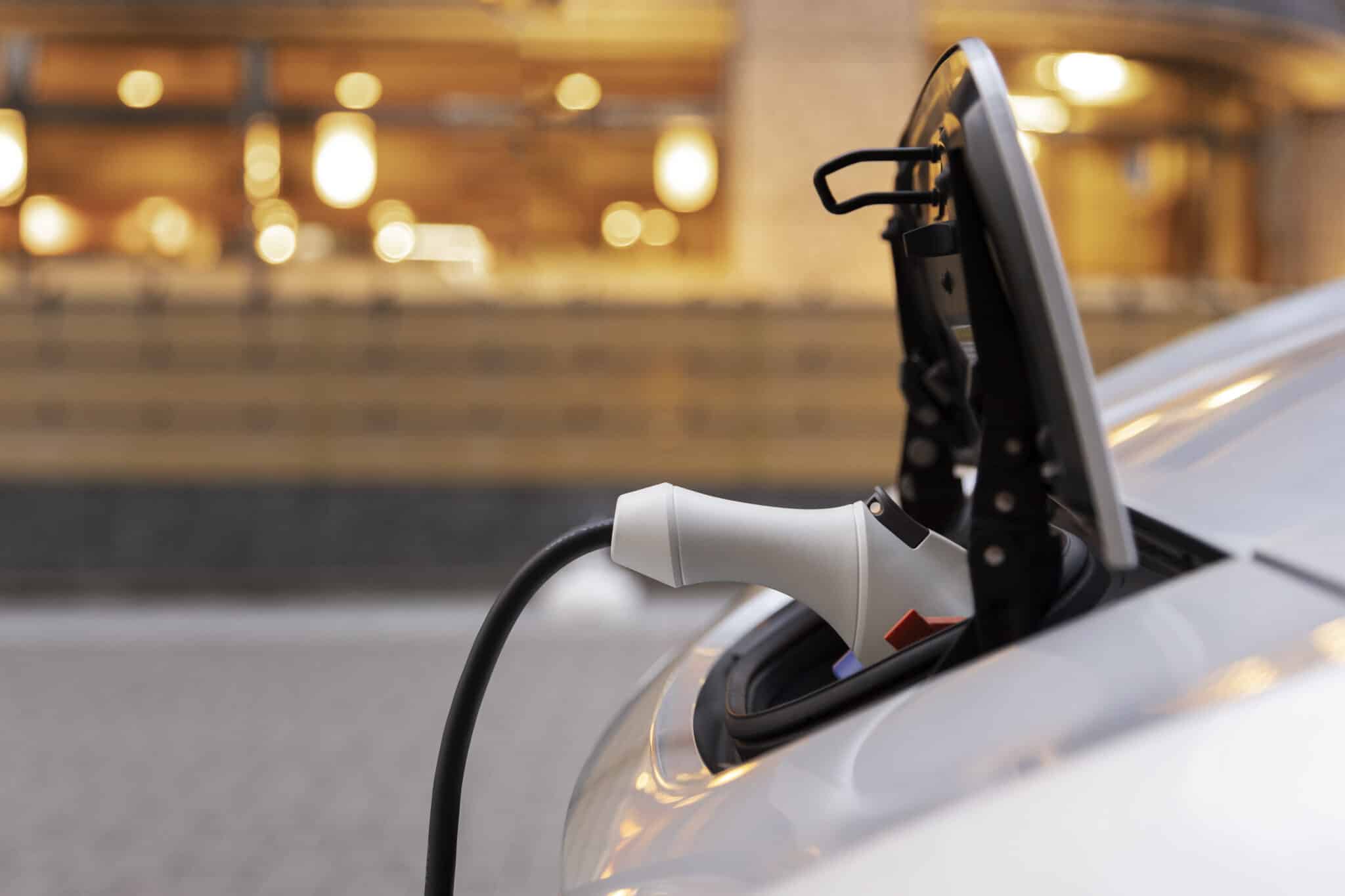 Prise de recharge branchée dans la trappe ouverte d'une voiture blanche devant une façade éclairée