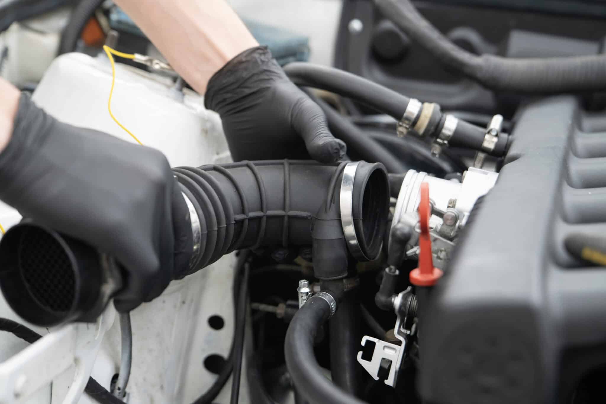 Mains gantées remontant une durite d'admission et ses colliers dans un compartiment moteur