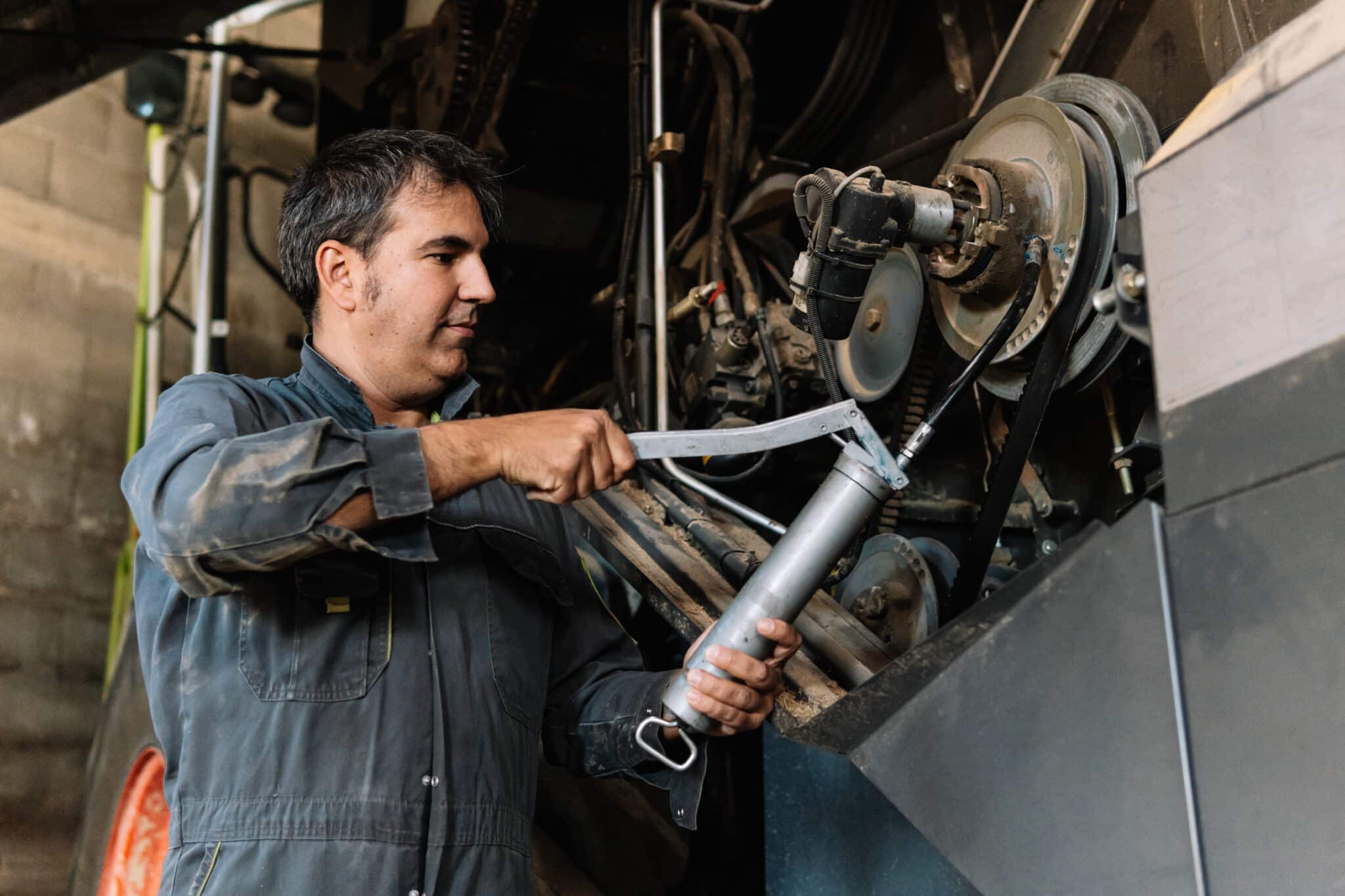 Homme en combinaison de travail graissant le mécanisme d'une grosse machine avec un pistolet à graisse